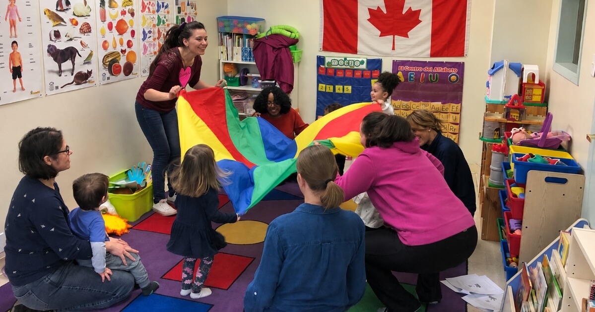 Children, parents and teachers enjoying an interactive Spanish class in Canada with a Canadian flag displayed in the classroom.